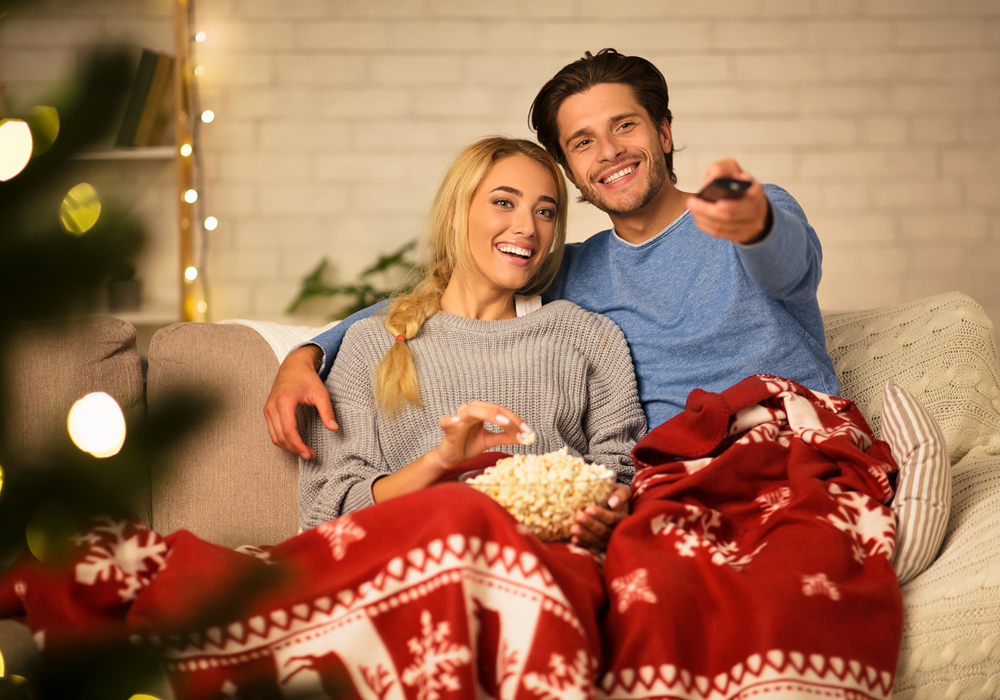 A couple eating popcorn and watching a movie on the couch.