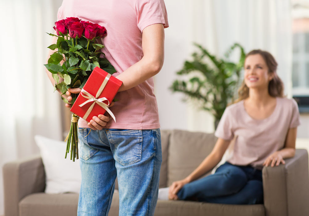 Man surprising woman with Valentine's Day gifts in apartment home.