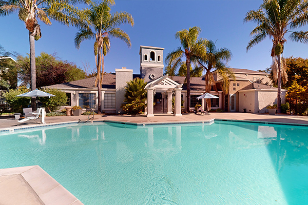 Outdoor swimming pool area with sundeck and lounge seating under pergola.