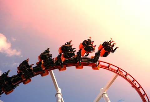 Roller coaster riders mid-air at sunset.