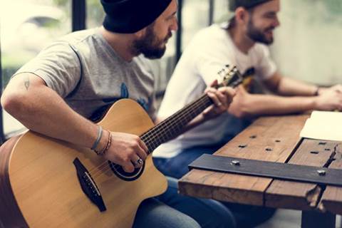 Man holding guitar sitting with another man.