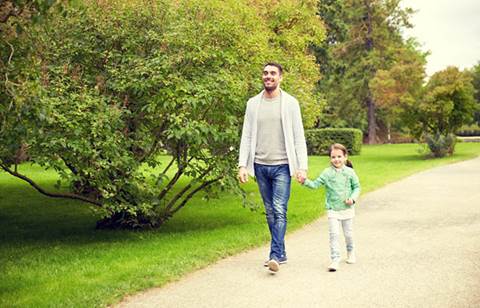 Man and boy walking hand-in-hand on path along lush landscaping.